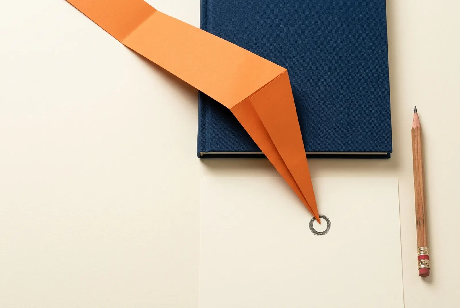 Orange paper strip crossing a dark notebook on a bright worktable